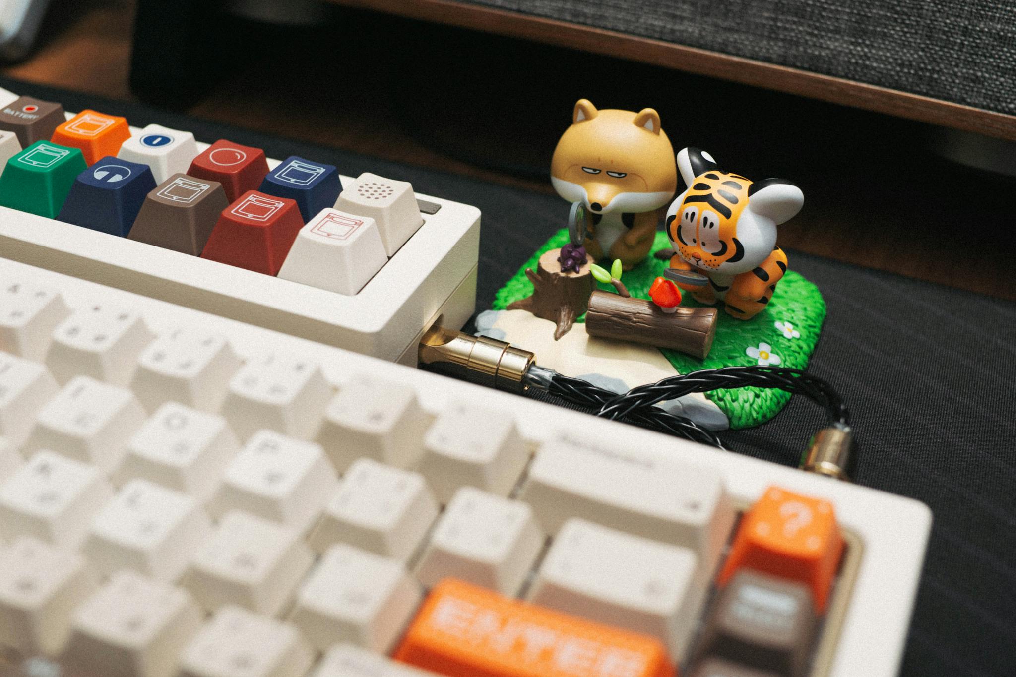 Mechanical keyboard with colorful keys and whimsical animal figurines on desk.
